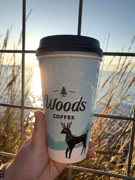 A picture of a Woods Coffee drink cup being held up to a window