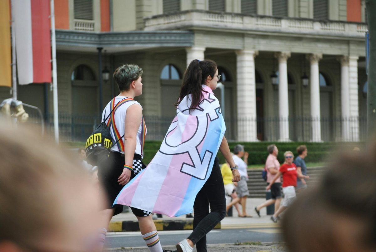 two people walking side by side, one of them is wearing a trans flag